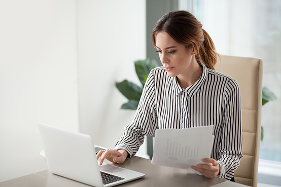 Woman sitting at desk with laptop holding papers