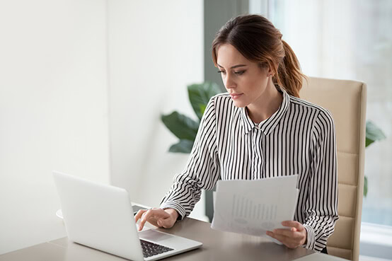 Consulting_DynamicForms Woman sitting at desk with laptop holding papers