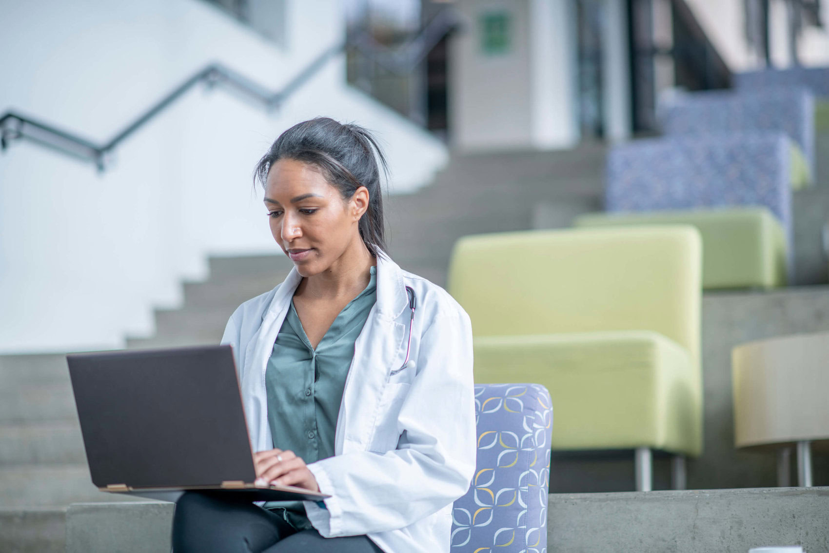 Medical student sitting in chair with laptop balanced on her knee